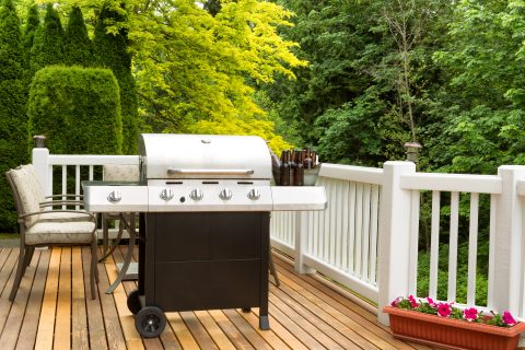 Clean barbecue cooker with cold beer in bucket on cedar deck. Table and colorful trees in background.